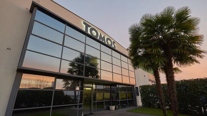 Exterior de la sede de TOMOS en Mazzano, con el rótulo de la empresa sobre la fachada acristalada